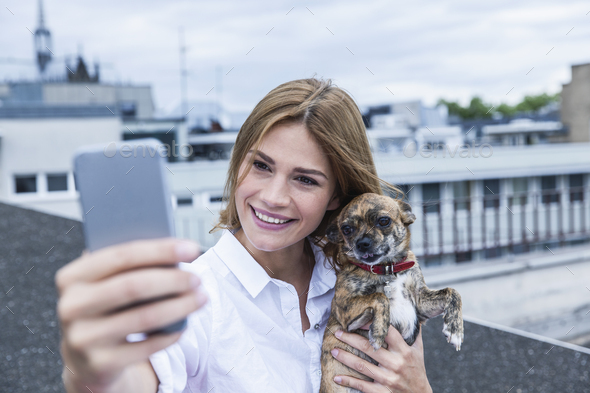 Portrait Of Smiling Young Woman Taking A Selfie With Her Dog On Roof 