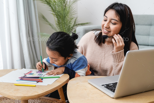 Happy asian mother working on computer at home with her child - Busy mom giving call center support