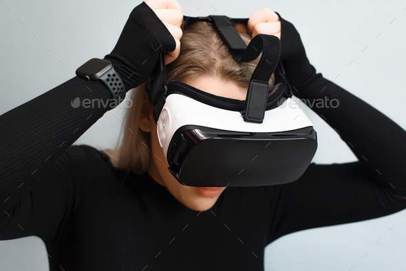 Young woman puts on virtual reality glasses, VR. Girl using interactive device, indoors. New