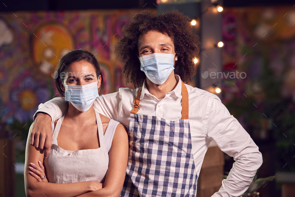 Portrait Of Male And Female Servers Working Night Shift In Bar Restaurant Or Club Wearing Face Masks