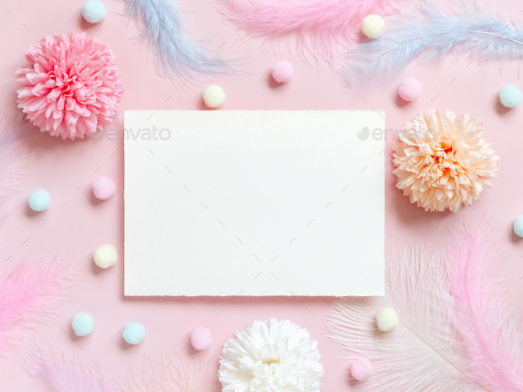 Blank card between pastel flowers, pom-poms and feathers near ring in a gift box on pink