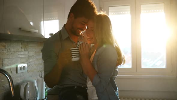 Beautiful Young Couple Hugging and Drinking Coffee in Kitchen
