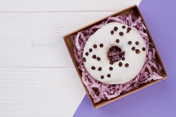 Box with decorated donut on color background.