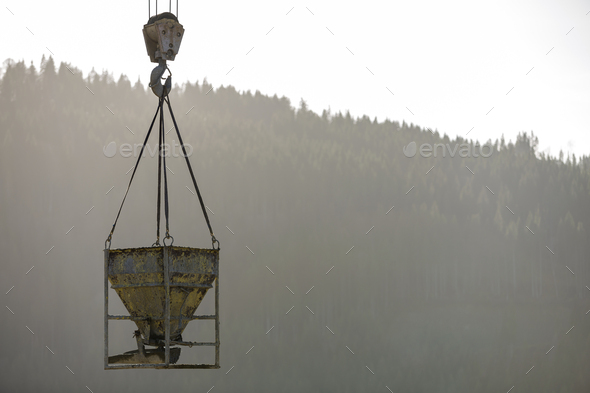 Bucket container with liquid concrete hanging on crane hook on copy space background. Construction