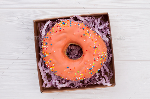 Donut in box on white wooden background.