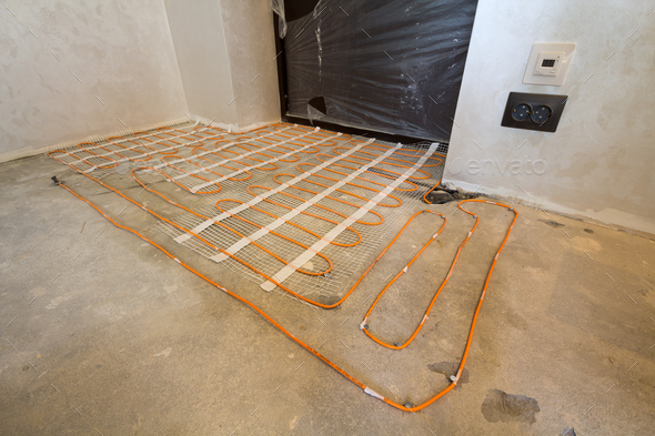 Heating red electrical cable wire system installed on cement floor in small new unfinished room with