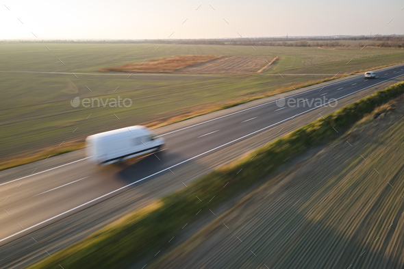 Aerial view of blurred fast moving cargo van driving on highway hauling goods. Delivery
