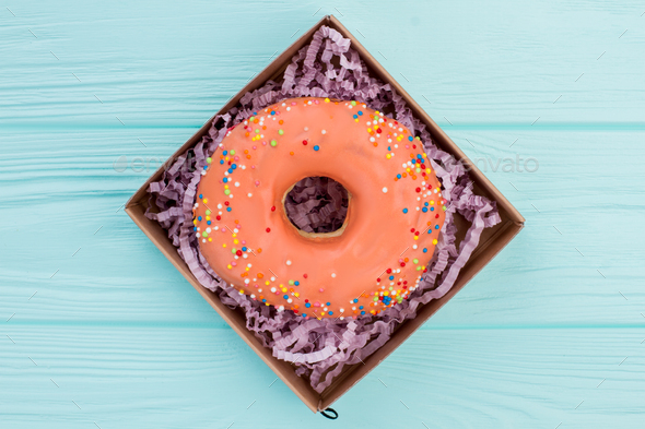 Donut with colorful sprinkles in box.