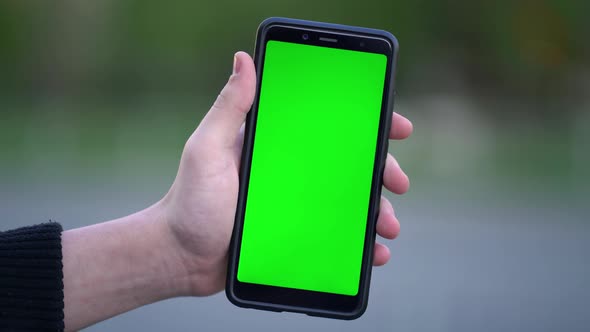 Man Holding Mockup Smartphone with Green Screen Outdoors on the Street alt