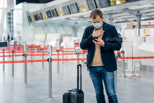 Businessman walks in airport terminal, has problems with breathing checks email box on smartphone