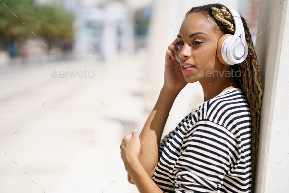 Young black woman listening to music with wireless headphones outdoors. - Stock Photo - Images