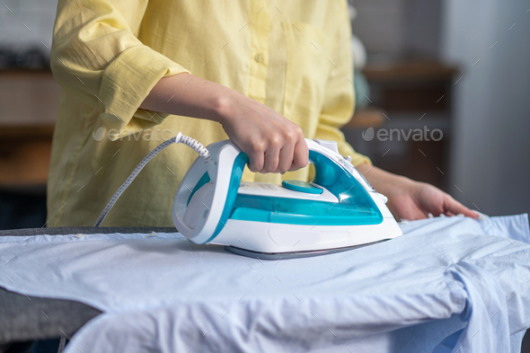 Female hands ironing wrinkled clothes on the ironing-board