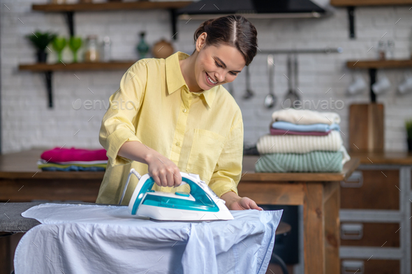 Girl smoothing out wrinkles on the shirt with a steam iron