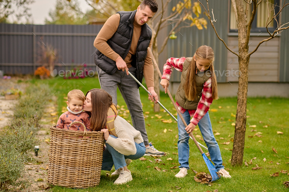 Man with girl raking leaves woman kissing child in basket