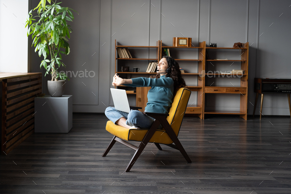 Young relaxed woman doing hand exercises at remote workplace, working during COVID-19 lockdown