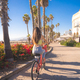 Attractive young woman riding bike near beach with palm trees - PhotoDune Item for Sale