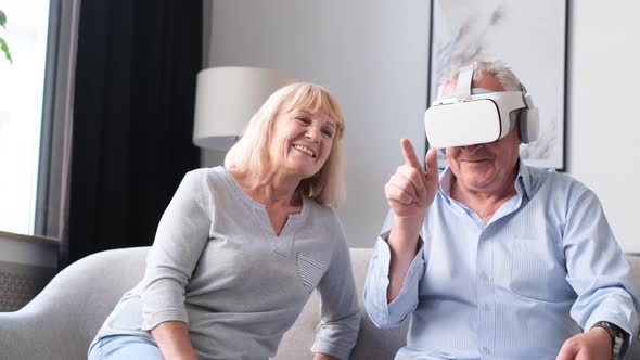 Portrait of Elderly Couple Using Virtual Reality Glasses While Sitting in Living Room alt