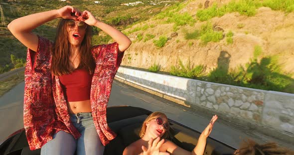 Beautiful brunette sitting on hood of convertible riding with her friends alt