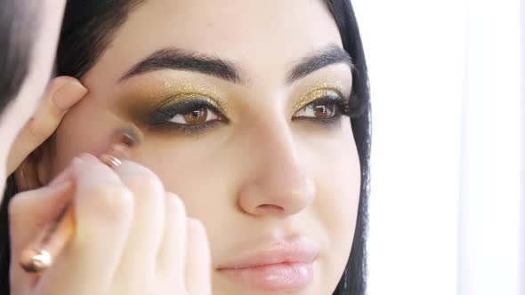 Girl Stylist Makes a Stylish Bright Makeup to a Young Beautiful Woman Model in the Studio alt