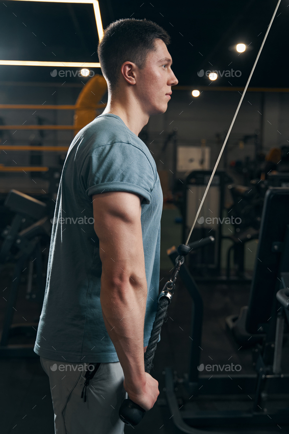 Concentrated athlete performing strength exercise on cable machine Stock Photo by Iakobchuk