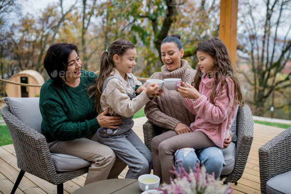 Two happy sisters with mother and grandmother sitting and drinking tea outdoors in patio in autumn - Stock Photo - Images