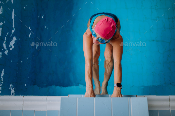 Top view of active senior woman swimmer holding onto starting block in indoors swimming pool
