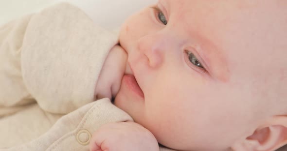 Closeup of a Cute Newborn with a Finger in His Mouth in the White Clothes