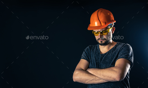 Male electrician in a protective helmet with glasses on a black background.