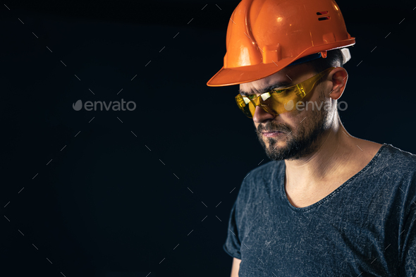 Male electrician in a protective helmet with glasses on a black background.