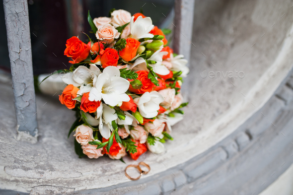 Wedding bouquet of white and orange roses and with two wedding rings on antique window