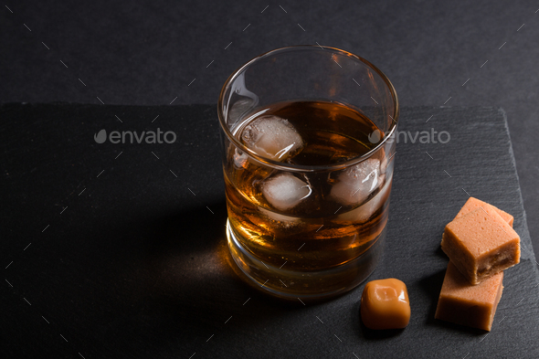 Glass of whiskey or bourbon with ice on black stone table., Stock image