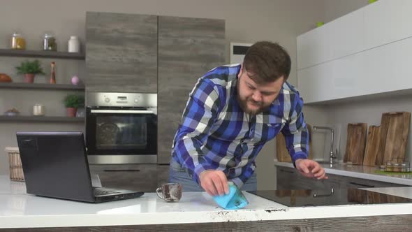 A Caucasian Man Cleans Up and Washes Spilled Coffee in the Kitchen, a Laptop, Slow Motion alt