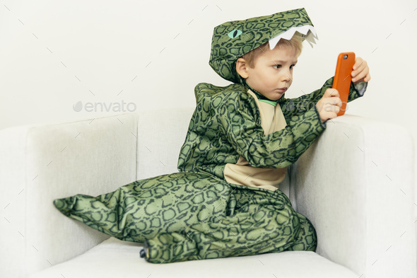 Little boy wearing dinosaur costume sitting on the couch with smartphone