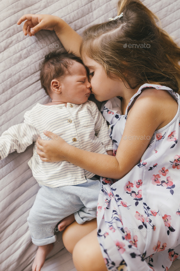 Affectionate girl lying on blanket cuddling with her baby brother Stock