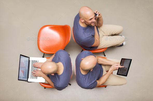 Man sitting on chairs using portable devices, multitasking
