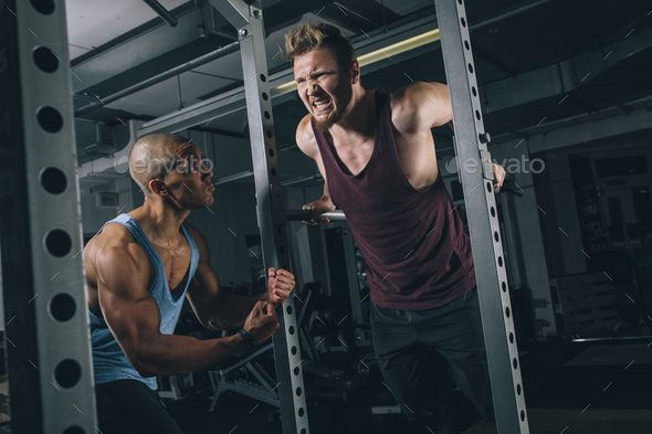 Two friends exercising dips at power rack in gym