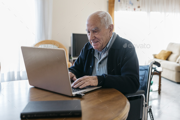Portrait of content senior man in wheelchair using laptop at home - Stock Photo - Images