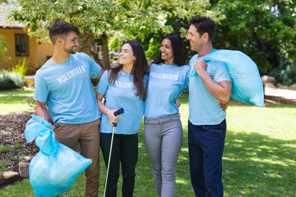 Happy multiracial volunteers collecting garbage in plastic bags during cleanup in park