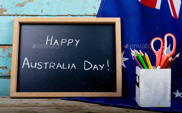 Writing slate with happy australia day text by desk organizer on flag over table