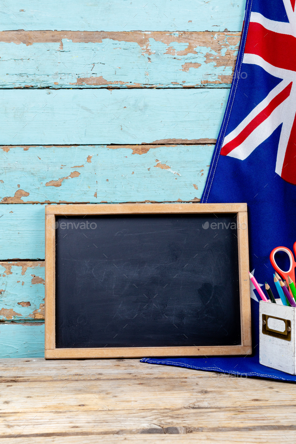 Blank writing slate by australian flag and desk organizer against old wooden wall with copy space