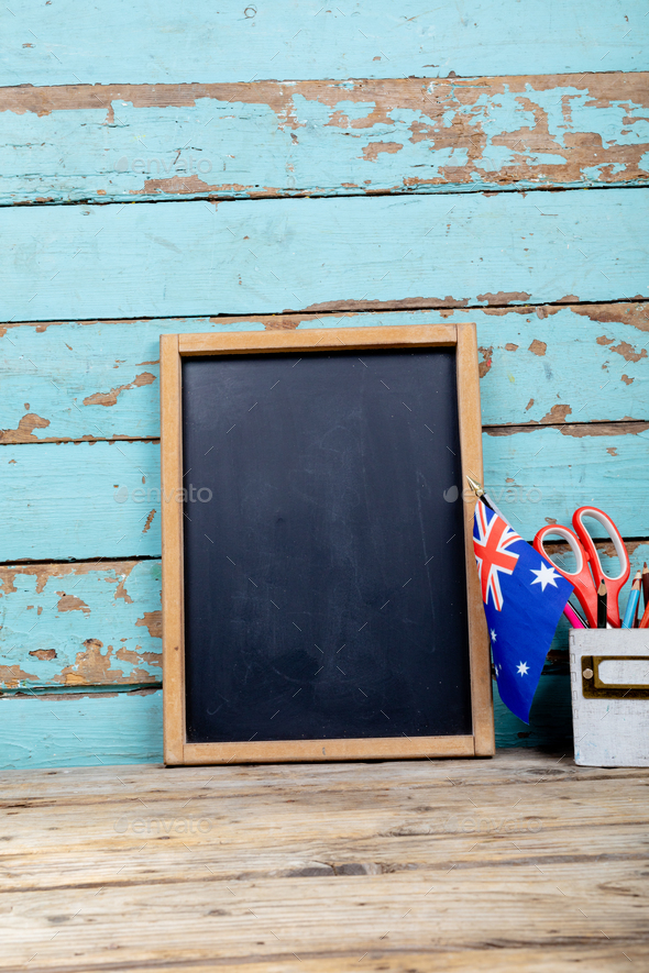 Blank writing slate by australia flag and desk organizer against blue wooden wall with copy space