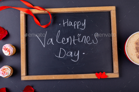 Happy valentines day text on writing slate by cupcakes and coffee cup on table