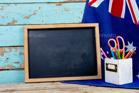 Blank writing slate by australian flag and desk organizer against blue wall with copy space