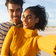 Portrait of smiling young beautiful biracial woman taking selfie with boyfriend at beach against sky - PhotoDune Item for Sale