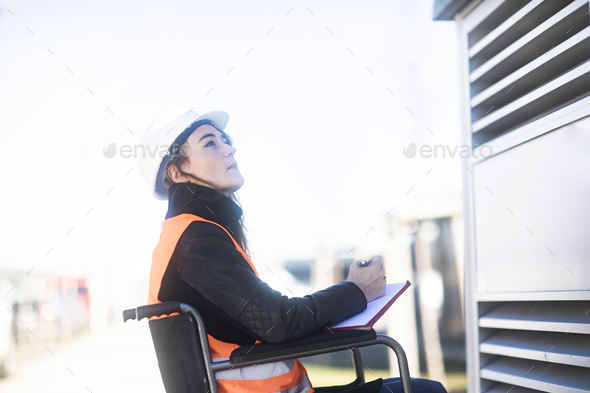 Young technician with safety helmet and vest in wheelchair working outdoors