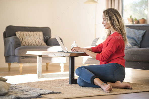 Woman using laptop on coffee table at home - Stock Photo - Images