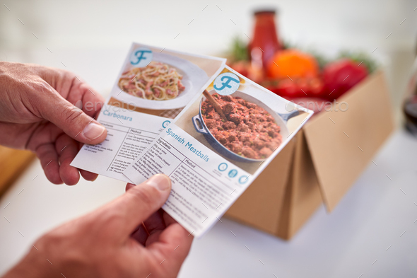 Close Up Of Hand In Kitchen Holding Recipe Cards For Online Meal Food Recipe Kit Delivered To Home