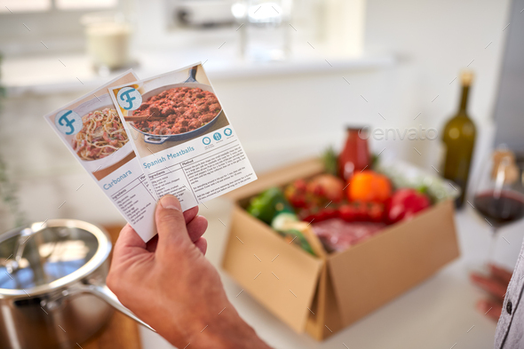 Close Up Of Hand In Kitchen Holding Recipe Cards For Online Meal Food Recipe Kit Delivered To Home