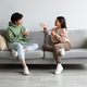 Young Asian boyfriend and girlfriend drinking coffee and chatting while sitting on sofa at home - PhotoDune Item for Sale