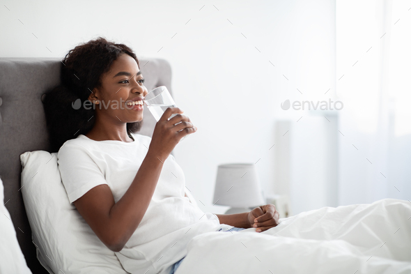 Pretty african american woman drinking water in bed